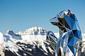 Close-up of mirrored bear sculpture with snow-covered mountain and blue sky in the background, Banff National Park; Banff, Alberta, Canada