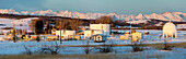Oil storage site with large spherical and round tanks with the warm light of sunrise in a snow-covered field with snow-covered  mountains and blue sky in the background, North of Longview; Alberta, Canada