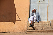 Eritreischer Mann sitzt auf den Stufen vor einer Tür; Asmara, Zentralregion, Eritrea