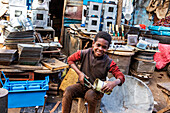 Eritreischer Junge beim Schneiden einer Dose auf dem Medeber-Markt, wo Kunsthandwerker alte Reifen und Dosen zu neuen Kunstgegenständen verarbeiten; Asmara, Zentralregion, Eritrea