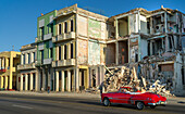An old car passes the demolished facade of old buildings along a street; Havana, Cuba