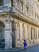 A woman walks on the street beside a building with ornate facade; Havana, Cuba