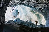 A woman takes a snapshot of Black Rapids Glacier from the entrance of an ice cave; Alaska, United States of America