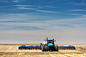 Traktor mit Einzelkornsämaschine bei der Aussaat eines Stoppelfeldes bei blauem Himmel und dunstigen Wolken, nahe Beiseker; Alberta, Kanada