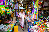 Buddhistische Nonne beim Einkaufen auf einem Markt, die Gegenstände in einem Korb auf dem Kopf trägt; Bagan, Region Mandalay, Myanmar