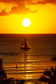 Golden sunset off Waikiki Beach with a silhouetted sailboat in the water; Honolulu, Oahu, Hawaii, United States of America