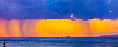 Storm clouds with rain and clouds glowing a bright yellow at sunset off Waikiki Beach with a silhouetted sailboats in the water; Honolulu, Oahu, Hawaii, United States of America