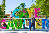 Touristen am bunten Schild von Caye Caulker; Belize