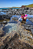 A young girl examines life in a tide pool beside Kawakiu Nui Beach on Molokai's West End; Molokai, Hawaii, United States of America