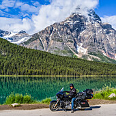 Man sitting on his motorcycle on the roadside of Icefield Parkway in front of Waterfowl Lakes; Improvement District No. 9, Alberta, Canada