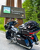 A motorcycle parked on the roadside of Bighorn Highway (Highway 40) in front of a sign for Kananaskis Country, Peter Lougheed Provincial Park; Alberta, Canada