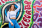 Portrait of a young woman standing against a wall of colourful street art; Wellington, North Island, New Zealand