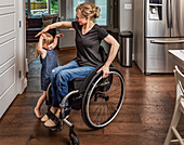 Eine querschnittsgelähmte Mutter tanzt mit ihrer Tochter in der Küche und benutzt dabei ihren Rollstuhl: Edmonton, Alberta, Kanada