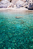 Female tourist floating on her back on the clear, turquoise water of Galazia Nera Bay; Polyaigos Island, Cyclades, Greece