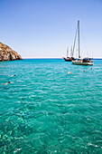 Touristen schwimmen im klaren, türkisfarbenen Wasser der Bucht von Galazia Nera, in der Segelboote vor Anker liegen; Insel Polyaigos, Kykladen, Griechenland