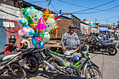 Mann steht neben einem Motorrad mit Luftballons; Manado, Nordsulawesi, Indonesien