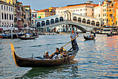 Gondolas and gondoliers in the Grand Canal with tourists along the colourful waterfront; Venice, Italy