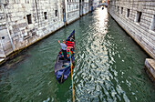 Gondoliere stehen auf einer Gondel im Kanal und unterhalten sich mit Touristen; Venedig, Italien