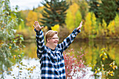 A young man with Down Syndrome raising his hands in worship to God, while in a city park on a warm fall evening: Edmonton, Alberta, Canada