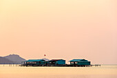 Erhöhte Gebäude auf dem Wasser während eines glühenden rosa Sonnenuntergangs, Starfish Beach; Phu Quoc, Provinz Kien Giang, Vietnam