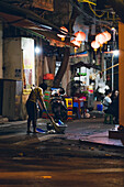 Woman sweeping up garbage in the street at night; Hanoi, Veitnam
