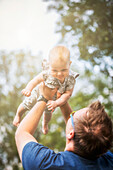 A father holding his baby girl in the air while outdoors during the fall; Edmonton, Alberta, Canada