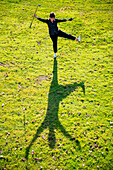 High angle view of female golfer on green grass holding her club and ball in the air and casting a shadow on the ground; Switzerland