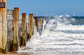 Waves splashing along the wooden wall at the shore and wind turbines in the distance in the water along the coast of Blyth; Blyth, Northumberland, England