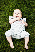 A contented little baby girl laying in the grass and smiling; Edmonton, Alberta, Canada