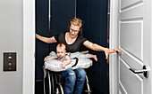 Eine querschnittsgelähmte Mutter hält ihr Baby auf dem Schoß, während sie mit ihrem Rollstuhl in den Aufzug ihres Hauses einsteigt: Edmonton, Alberta, Kanada