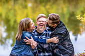 A young man with Down Syndrome being teased and hugged by his father and mother while enjoying each other's company in a city park on a warm fall evening: Edmonton, Alberta, Canada