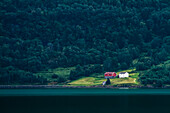 Isoliertes norwegisches Haus an einem See, umgeben von einem dunklen Wald; Norwegen