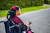 Maori-Frau mit Cerebralparese in einem Rollstuhl, die einen Bürgersteig entlangfährt; Wellington, Neuseeland