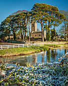 Shanrahan Church, an old church ruins framed by big trees covered in frost in the morning with a river in the foreground; County Tipperary, Ireland