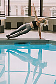 Woman working out on a mat doing a side plank at the edge of a pool; Wellington, New Zealand