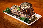 Close-up of decorative log cake with pine needle trimmings on a wooden table; Studio