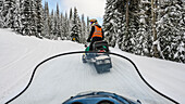 Schneemobil fährt im Winter einen Waldweg hinunter; Sun Peaks, British Columbia, Kanada