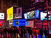 Times Square advertisements illuminated at night with tourists lining the street, Midtown Manhattan; New York City, New York, United States of America