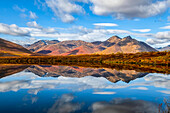 Fall colours ignite the landscape of the Dempster Highway with vibrant colours reflected as a mirror image in a tranquil lake; Dawson City, Yukon, Canada