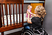A paraplegic mother picking her baby up after a sleep in a customized crib with a sliding door; Edmonton, Alberta, Canada