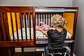 A paraplegic mom putting her baby down to sleep in a customized crib with a sliding door; Edmonton, Alberta, Canada