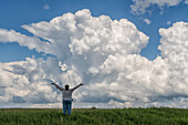 Erstaunliche Wolken über der Landschaft des Mittleren Westens der USA, während sich Superzellengewitter entwickeln. Eine Person steht mit erhobenen Armen im Vordergrund; Nebraska, Vereinigte Staaten von Amerika