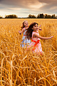 Zwei junge Mädchen rennen in einem goldenen Weizenfeld; Alberta, Kanada