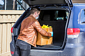 Ein junger Mann lädt während der Covid-19-Weltpandemie Lebensmittel in den Kofferraum seines Fahrzeugs; Edmonton, Alberta, Kanada