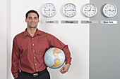 Geschäftsmann hält Globus und steht neben Uhren mit internationalen Zeitzonen