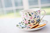 Teetasse in hübscher Blumentasse und Untertasse mit Keksen, Atelieraufnahme