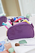 Women's toiletry and cosmetic travel bag on bathroom counter, filled with toothbrush, lotion, makeup and other beauty products, USA