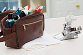 Men's toiletry travel bag on bathroom counter, filled with toothbrush, lotion, razor and other grooming products, USA