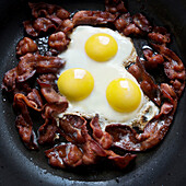 greasy frying pan full of bacon and eggs
