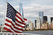 Amerikanische Flagge auf einer Fähre mit dem One World Trade Center und der Skyline im Hintergrund, New York City, New York, USA